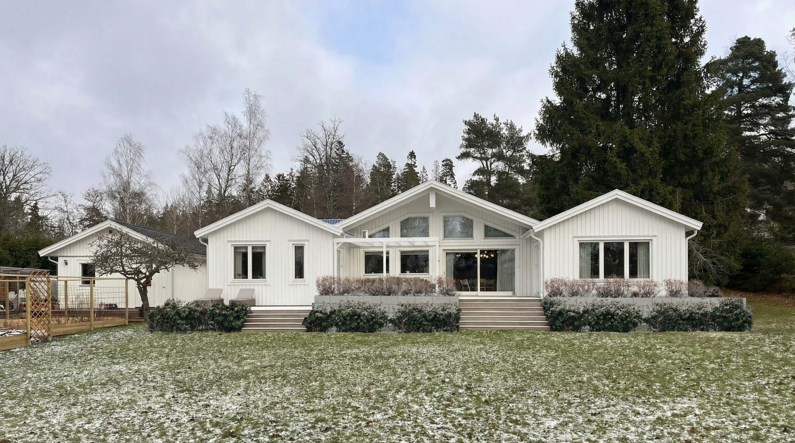 Vitt trähus med stora fönster och snöig gräsmatta